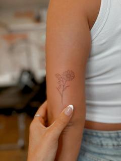 Fine line daisy lily tattoo by @emmathornetattoo