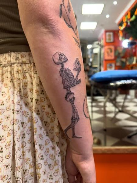 Fine line skeleton reading tattoo by @gayle.inklore